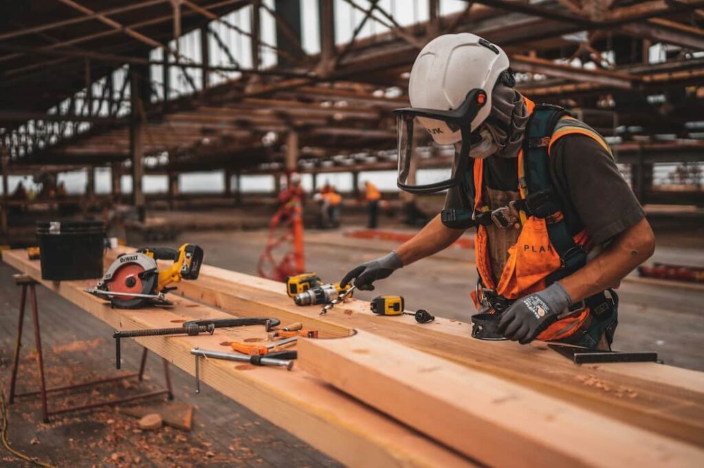 Construction worker in a hard hat and face shield measuring timber on site