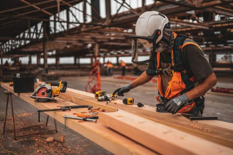 Construction worker in a hard hat and face shield measuring timber on site
