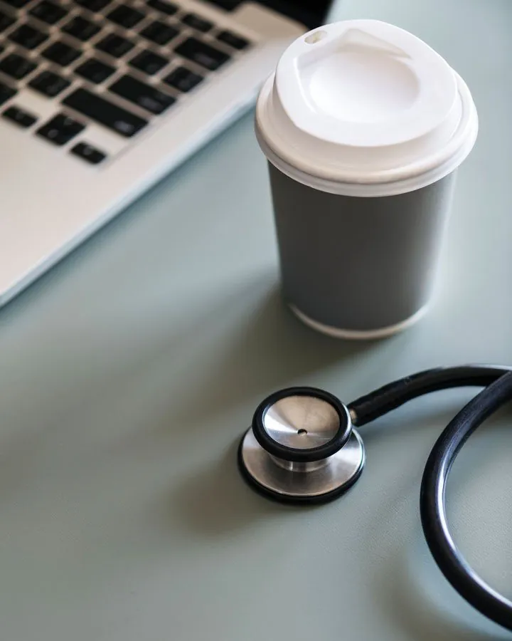 Stethoscope beside a coffee cup and laptop