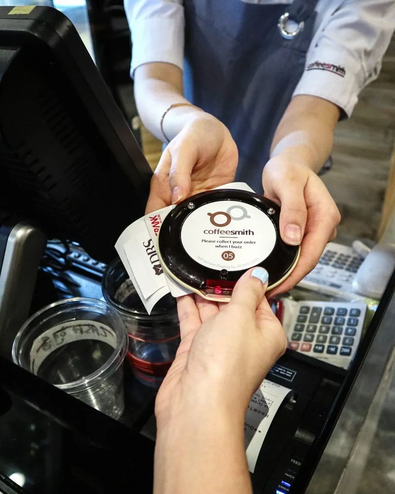 Cashier handing a customer pager across a cafe counter