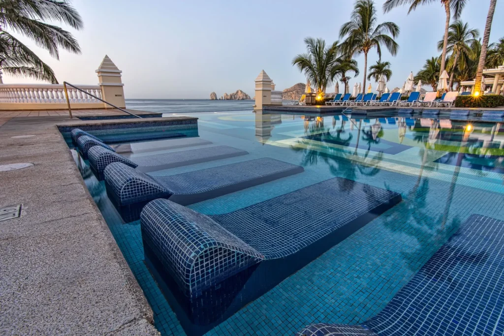 Resort pool deck with sun loungers and palm trees at dusk