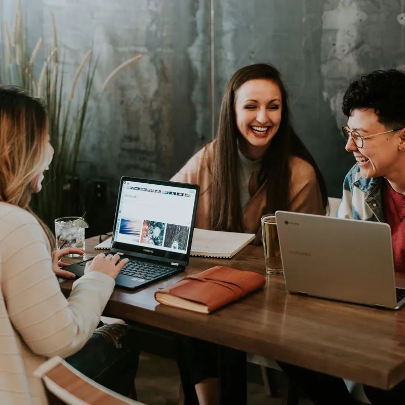 Friends laughing over laptops at a cafe table