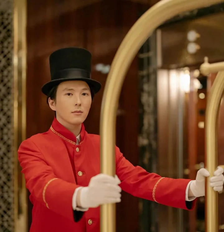 Hotel bellboy in a red uniform beside a luggage cart